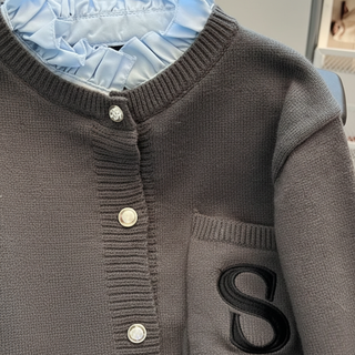 Close-up of a brown cardigan with buttons and a letter 'S' on a light blue background