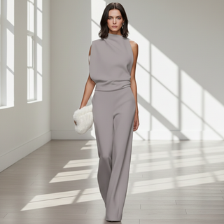 Woman in a gray outfit standing in a bright room with sunlight streaming through windows.