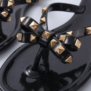 Extreme close-up of a black jelly sandal showing the metallic gold pyramid studs on a decorative bow strap.