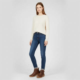 Woman wearing a cream sweater, blue jeans, and brown boots on a white background