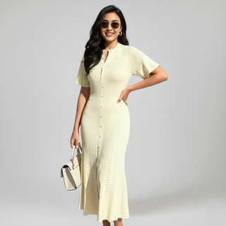 Beige knit dress with a flowing silhouette and short sleeves, worn in a sun-drenched interior.