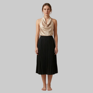 Woman wearing a beige sleeveless top and black pleated skirt on a beige background