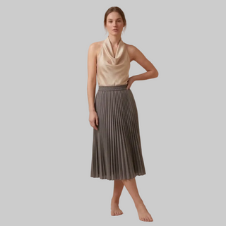 Woman wearing a beige sleeveless top and gray pleated skirt on a beige background