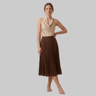 Woman wearing a beige sleeveless top and brown pleated skirt on a beige background