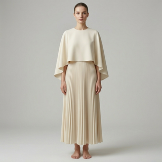 High-fashion editorial photo of a cream-colored two-piece set featuring a cropped cape top and a high-waisted pleated skirt.