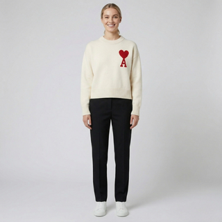 Minimalist studio shot of a cream-colored sweater with a red heart logo paired with black trousers.