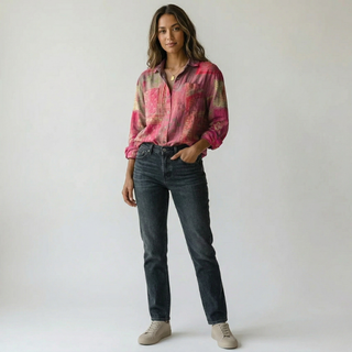 Model posing in a pink patterned long-sleeve blouse tucked into dark slim-fit jeans.