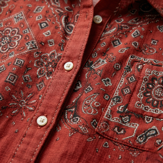 Close-up of the fabric, white buttons, and dark floral embroidery on a rust red cotton shirt.
