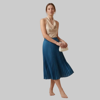 Woman wearing a beige top and blue pleated skirt on a beige background